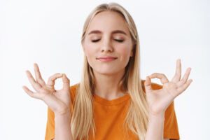close up peaceful determined sound minded good looking blond girl orange t shirt close eyes making zen gestures meditating close eyes smiling relieved making yoga breathing practice
