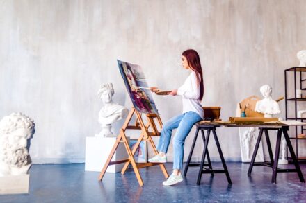 a woman sitting on a stool painting a picture