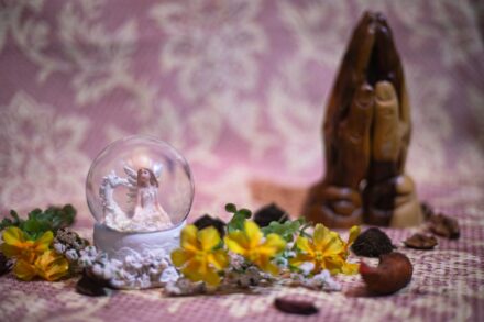 A snow globe and praying hands rest together.