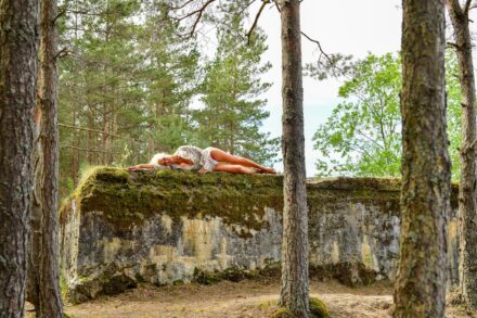 Holistic Healing Woman resting on moss-covered concrete structure in forest.