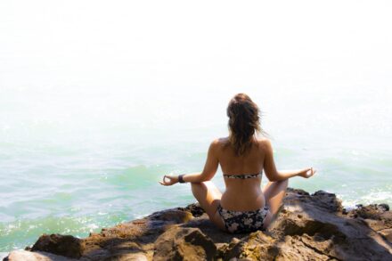 woman in black and white bikini standing on rock near sea during daytime