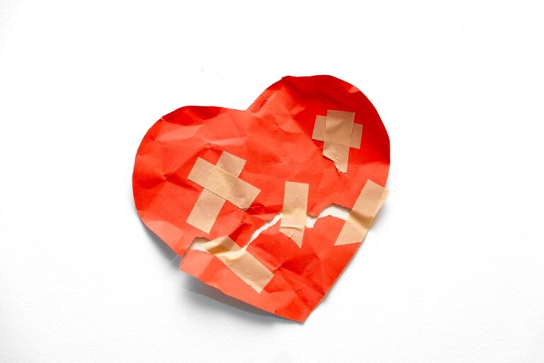 A broken red heart taped together on white background