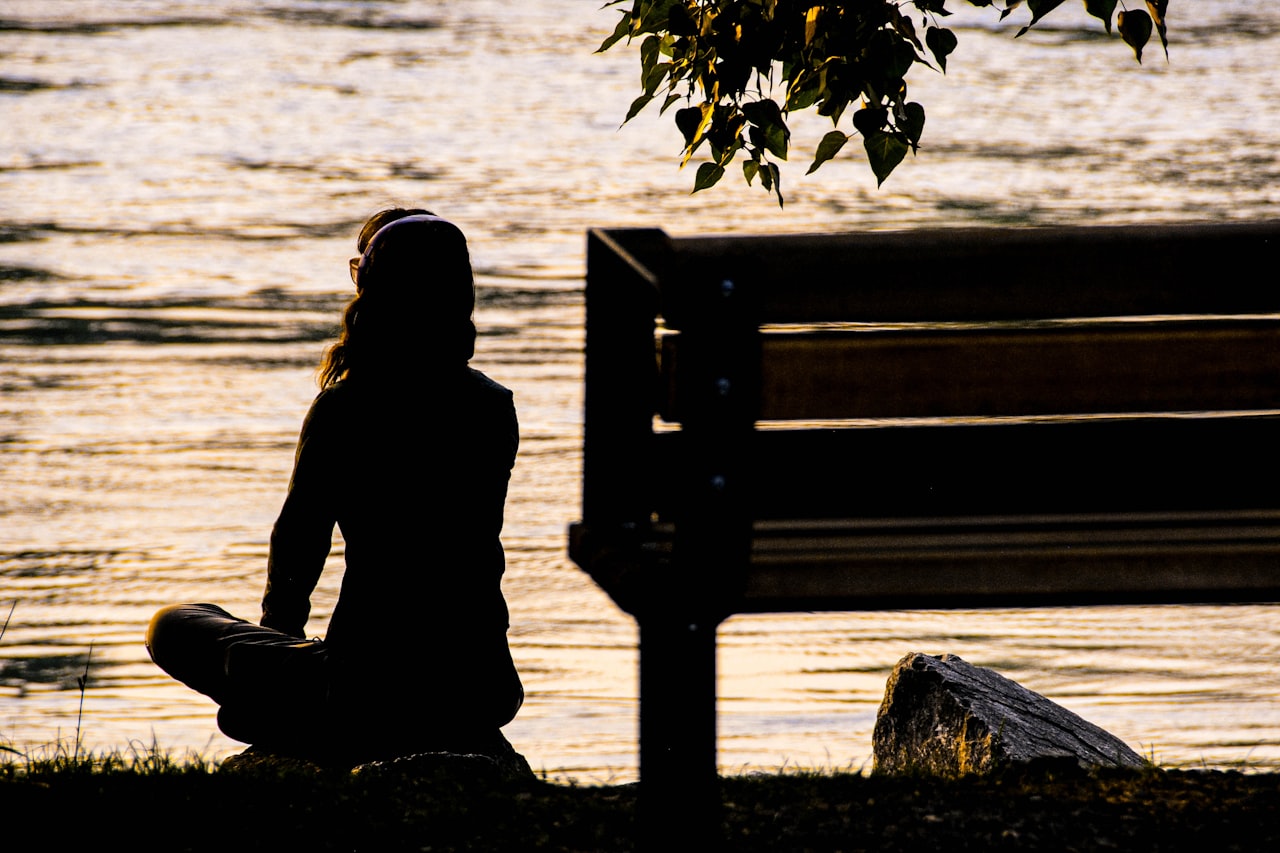 Mindful Living & Healing 1 Silhouette of a person sitting beside the water at dusk in mindful reflection