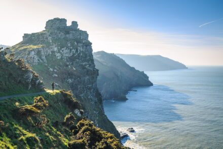 Mind-Body Healing person standing near road viewing cliff and sea under blue and white skies