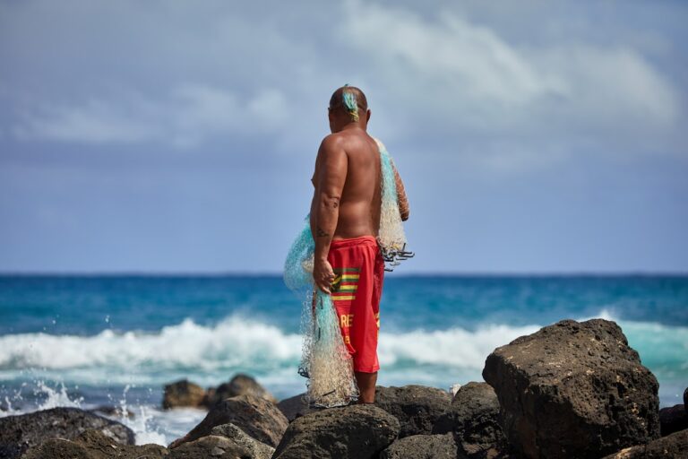 A fisherman stands gazing at the ocean.
