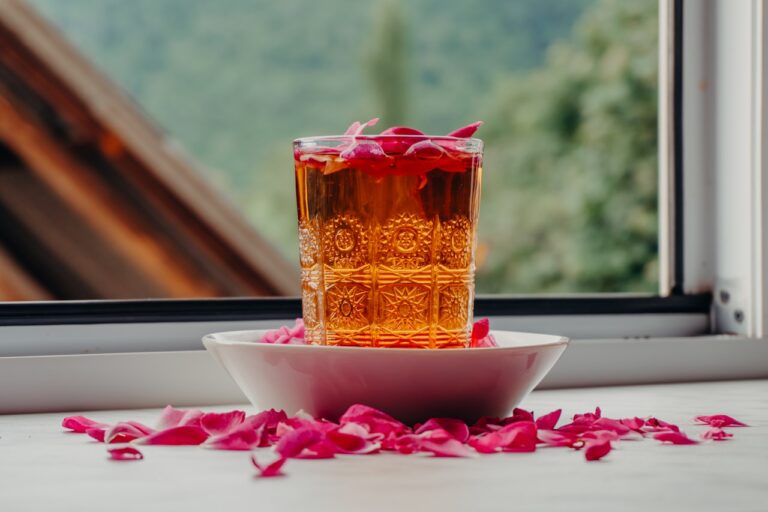 Glass of tea with rose petals on windowsill