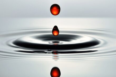 Red liquid drops falling into water surface