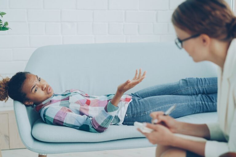 Quantum Healing & Techniques Therapist listens to young woman on couch.