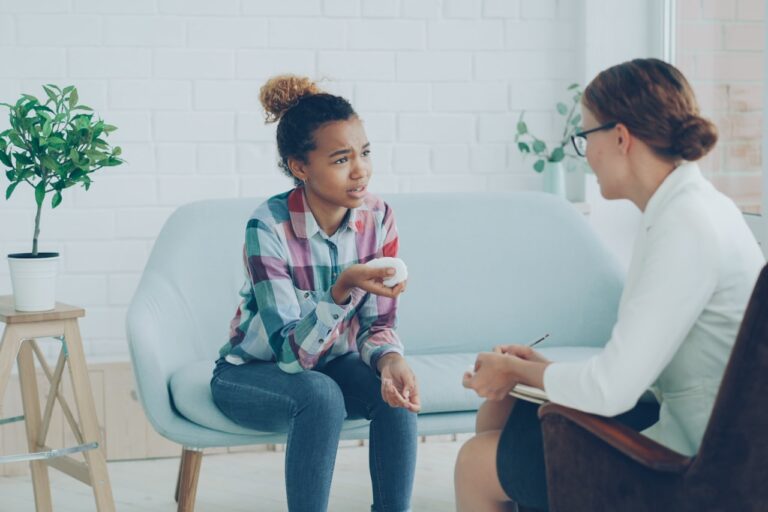 Quantum Healing & Techniques Therapist talking to a young girl on couch.