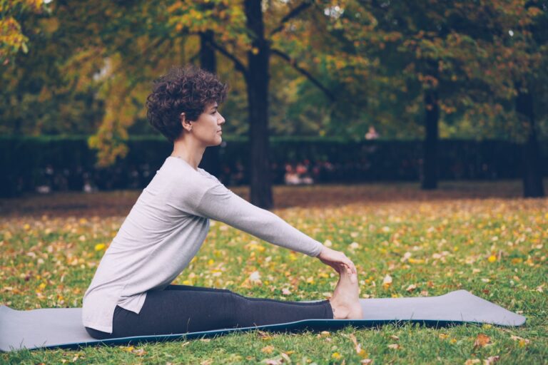 Quantum Healing & Techniques Woman stretching on yoga mat in autumn park.