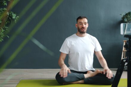 Man meditating on yoga mat recording with phone.