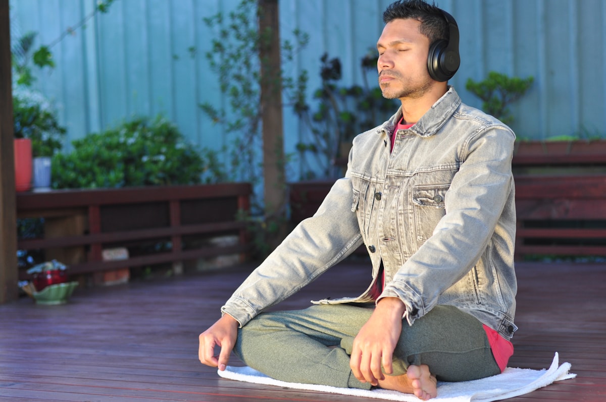 Man practicing somatic healing seated cross-legged outdoors with headphones and eyes closed