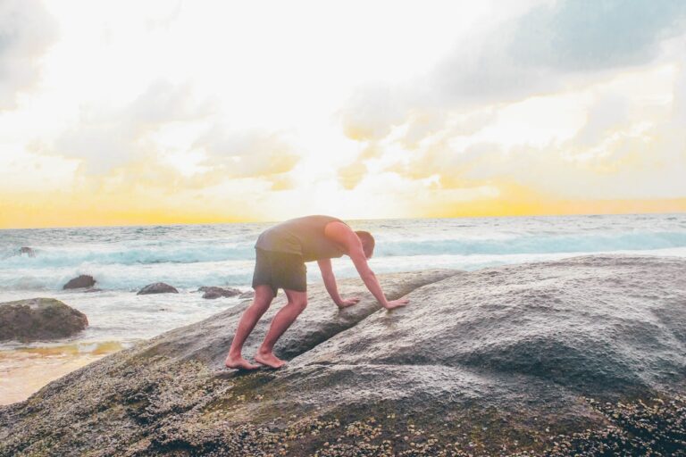 Yoga man on gray rock near body of water