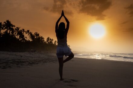 Yoga woman in white tank top and white shorts standing on beach during sunset